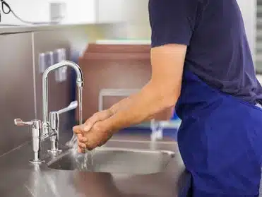 Nurse rinsing hands under a faucet in a medical setting.