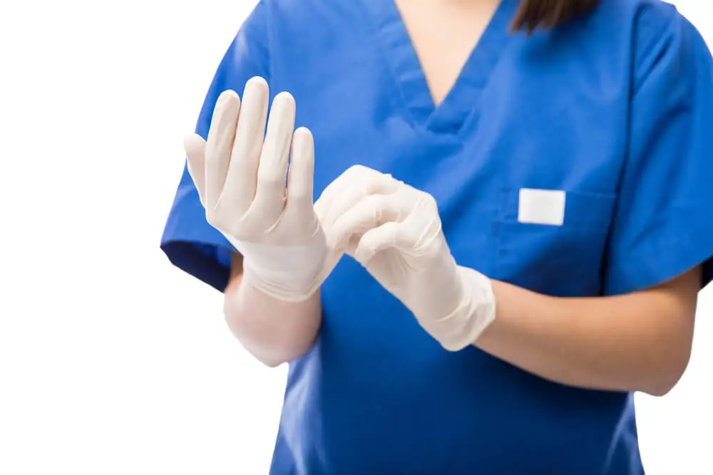 A medical professional in blue scrubs wearing and adjusting white gloves.